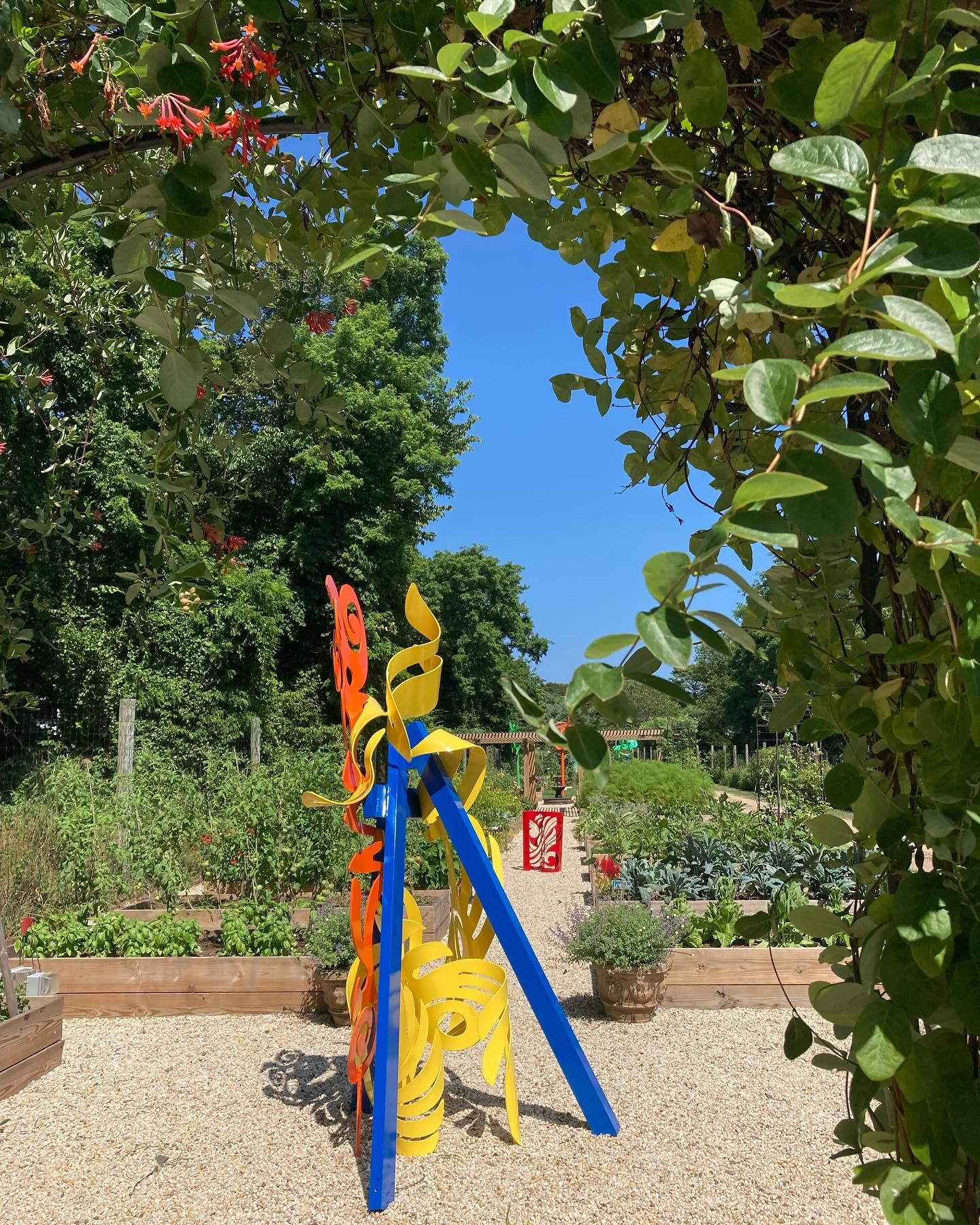 A painted sculpture seen through the honeysuckle arch